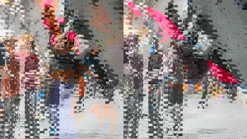 Indoor climbing wall at The Prop Store in Glasgow, with a climber tackling a bouldering problem on bright pink holds while others watch from below.