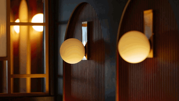 Modern wall sconces with round frosted glass globes mounted on arched wooden panels, illuminated with warm ambient light.
