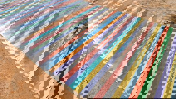 A long pathway is made of colourful vinyl strips, each one listing a band name and a date. The strips are arranged side-by-side to create a vibrant, textured surface.