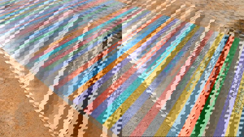 A long pathway is made of colourful vinyl strips, each one listing a band name and a date. The strips are arranged side-by-side to create a vibrant, textured surface.