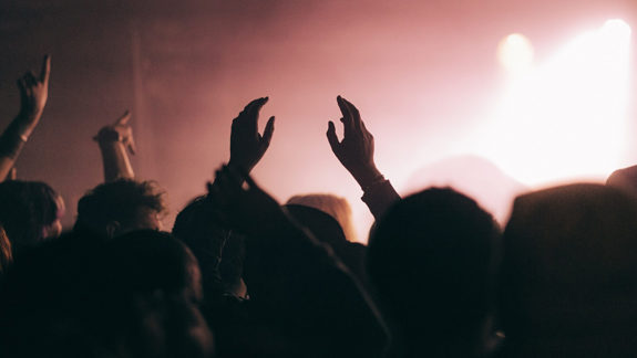 Audience with raised hands silhouetted against pink stage lighting at a packed Glasgow gig.