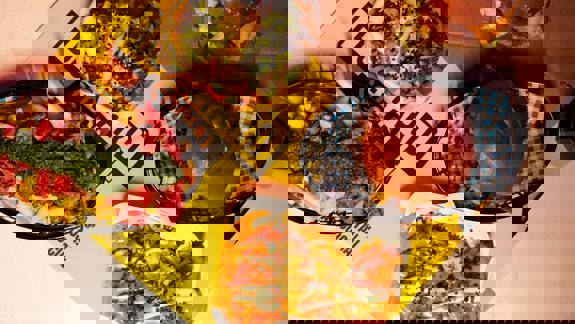 Top-down view of burgers, loaded fries, chicken tenders, and sauces on a table with bright yellow “Dockyard Social” placemats. Casual, colourful street food spread.