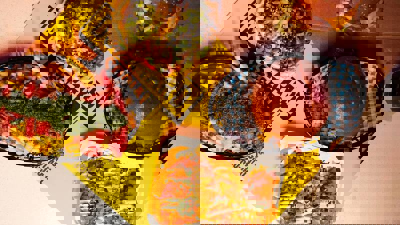 Top-down view of burgers, loaded fries, chicken tenders, and sauces on a table with bright yellow “Dockyard Social” placemats. Casual, colourful street food spread.