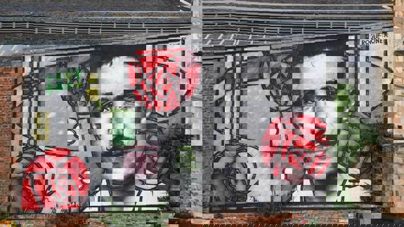 Mural of Charles Rennie Mackintosh in a stained-glass style with red roses on a building.