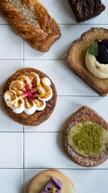 A collection of pastries and baked goods on a white tiled surface, including a meringue tart and a pistachio danish.