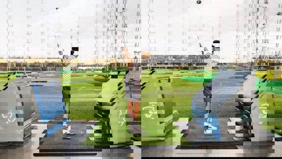 Golfer swinging at Topgolf Glasgow driving range with modern practice bays and colourful targets on the field.