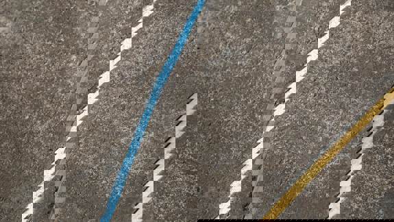 A close-up of a concrete surface with painted lines in blue, white, and gold intersecting.