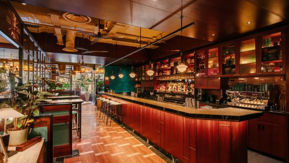Warm and stylish bar interior with wooden furnishings, hanging lights, and a long counter at Dishoom restaurant in Glasgow