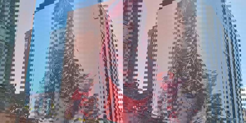 A large, colourful mural on the side of a building, depicting a person with pink hair holding a cocktail and a candle.