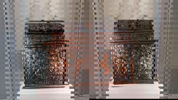 A close-up of a carved wooden writing casket on a white display pedestal.