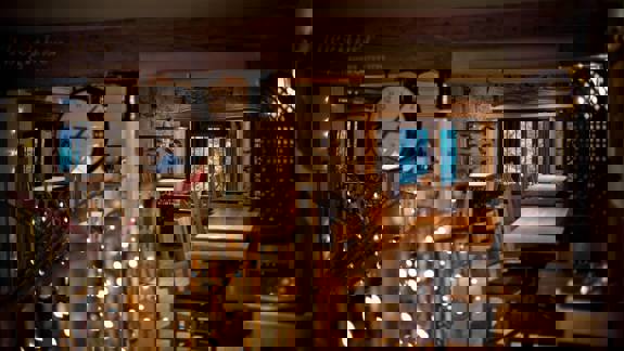 Interior of Stravaigin restaurant with warm lighting from fairy lights and windows, wooden tables and chairs, and a prominent clock, suggesting a cosy, rustic feel.