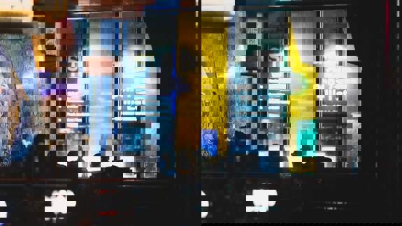 Dark interior view of Nice N Sleazy in Glasgow with dimly lit patrons and a bright, colourful window sign.