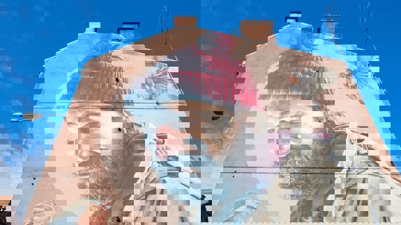 Mural on a gable end showing a man known as St Mungo with a beard and red bobble hat looking down at a robin.