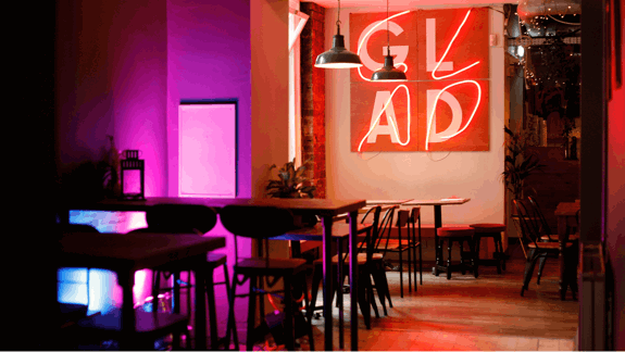 An interior shot of a restaurant with a large neon sign that reads 'GLAD' and empty tables.