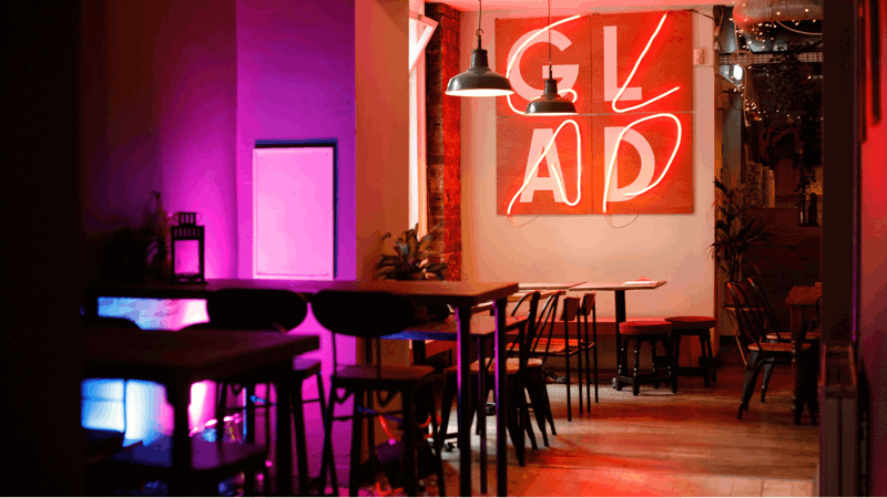An interior shot of a restaurant with a large neon sign that reads 'GLAD' and empty tables.