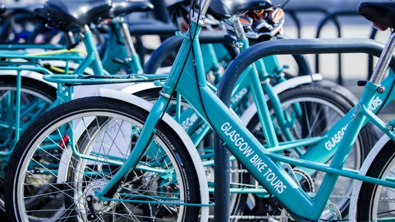 A close-up shot of a row of bright turquoise bicycles, with "Glasgow Bike Tours" written on the frame of the bike in the foreground.