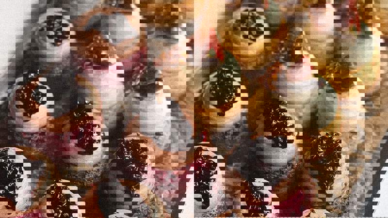 A close-up of a tray of elegant mini cakes. Some have blueberry topping, others are topped with a creamy swirl and fig pieces.