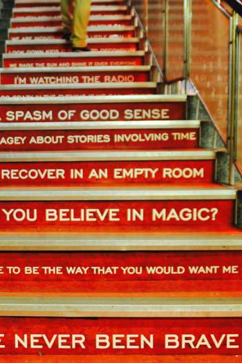 An interior view of red stairs, each riser painted with white song lyrics from the band Biffy Clyro, including "I'll recover in an empty room."