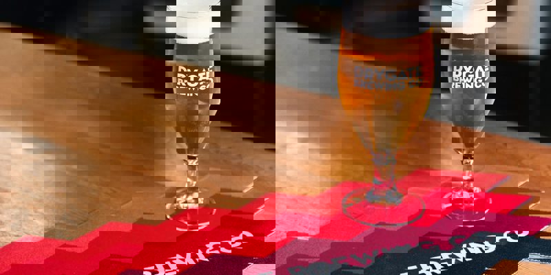 A glass of beer on a wooden table with a runner that says "Drygate Brewing Co."