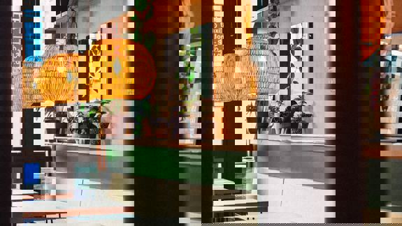 An interior view of a restaurant with a colorful design, hanging plants, and woven light fixtures.