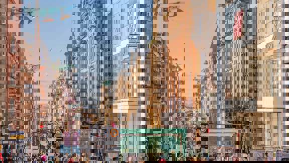 Buchanan Street, Glasgow, bustling with shoppers under a clear sky, featuring historical architecture, modern shopfronts like H&M, and a Subway entrance.