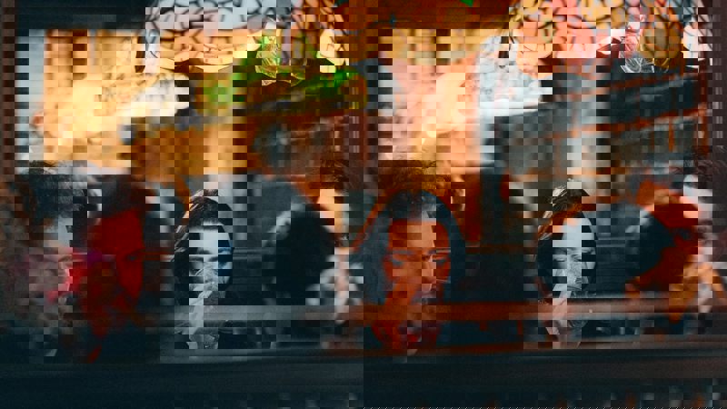 A group of people sitting at a booth-style table in a dimly lit bar with a stained-glass lampshade hanging above them.