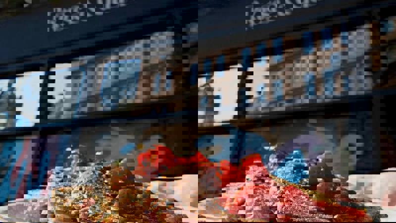 Close-up of a plate of French toast topped with strawberries, held in front of a cafe with a sign reading "Rose & Grants."