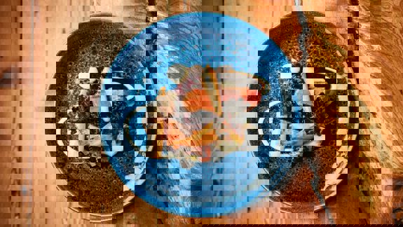 An overhead shot of a blue ceramic plate with a gourmet meal on a rustic wooden table.