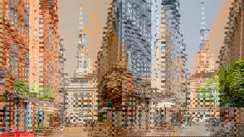 A wide street view showing historic architecture in Glasgow, including a church with a tall steeple and clock face, and several cafes