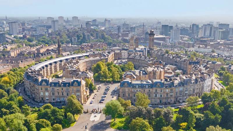 An aerial view of Park Circus, a crescent of historic buildings surrounded by green parkland in Glasgow.