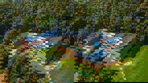 An aerial view of the Burrell Collection museum, a modern building with a glass roof, surrounded by a lush green forest.