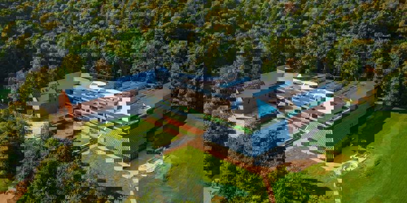 An aerial view of the Burrell Collection museum, a modern building with a glass roof, surrounded by a lush green forest.