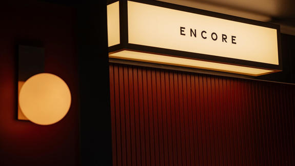 A rectangular, glowing "ENCORE" sign hangs above a textured red wall. To the left, a spherical light fixture emits a soft, warm glow