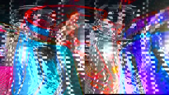 Four individuals are seated and laughing in a bright blue, spinning fairground ride compartment at the Irn Bru Carnival.