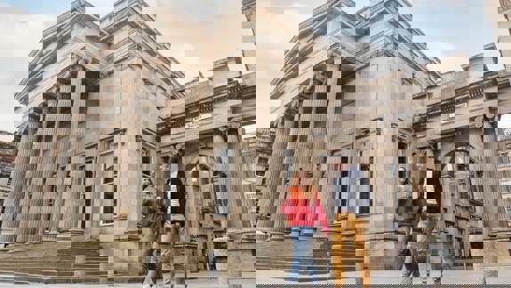 A couple walks past the Royal Exchange Square building in Glasgow, with its grand classical columns.