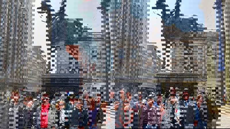 A group of people gathered in front of a statue with a traffic cone on its head.