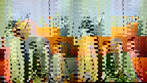 Four men in suits sitting on a red couch around a small table with pints of stout on it.