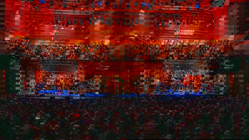 A performance hall with a large choir on risers and a group of musicians on stage, performing for a seated audience.