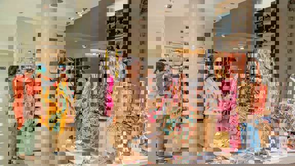 Visitors browse beautiful, brightly coloured gifts and souvenirs in a well-lit museum shop. Textiles, jewellery, and bags are displayed for purchase.