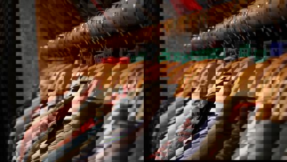 A close-up, angled shot of men's shirts hanging neatly on wooden hangers in a row on a wooden rail. The hangers have green plastic size markers (M and L) visible.