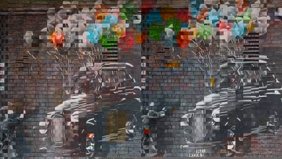 Mural of a black taxi cab floating with balloons, as a man reaches out to it.